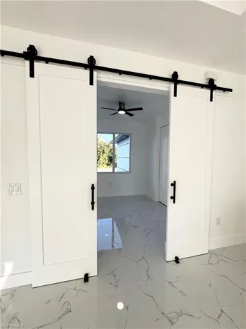 Unfurnished room featuring a barn door, light marble finish flooring, and a ceiling fan