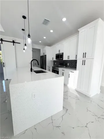 Kitchen featuring a barn door, light marble finish floors, hanging light fixtures, stainless steel appliances, and light stone counters
