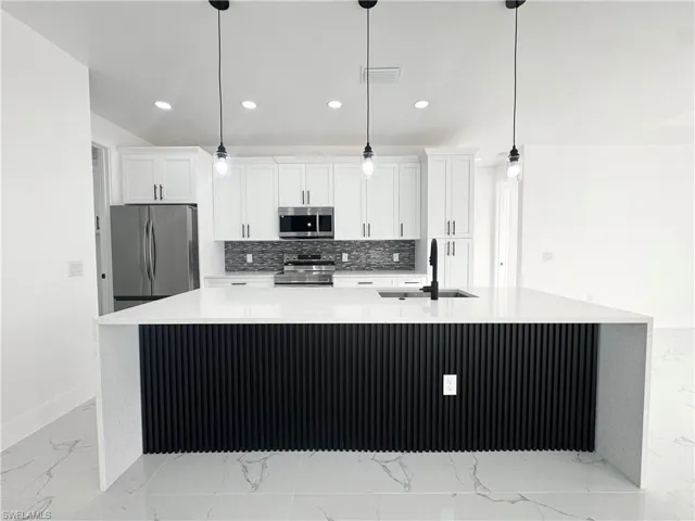 Kitchen featuring light stone countertops, a spacious island, light marble finish floors, stainless steel appliances, and recessed lighting