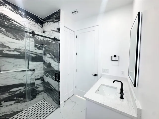 Bathroom with double vanity, light marble finish floors, and a marble finish shower
