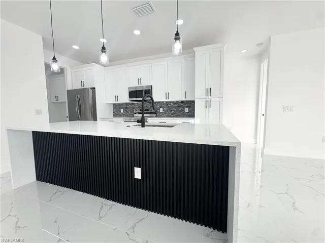 Kitchen featuring light stone countertops, stainless steel appliances, white cabinets, light marble finish floors, and recessed lighting