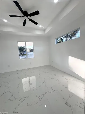 Empty room featuring light marble finish flooring, recessed lighting, a ceiling fan, and a raised ceiling
