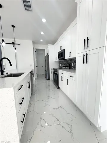 Kitchen featuring stainless steel appliances, light marble finish floors, light stone countertops, white cabinets, and recessed lighting