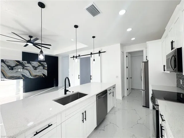 Kitchen featuring a barn door, white cabinetry, recessed lighting, light stone counters, and pendant lighting