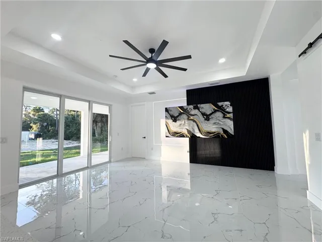 Empty room with a barn door, light marble finish flooring, an accent wall, a ceiling fan, and recessed lighting