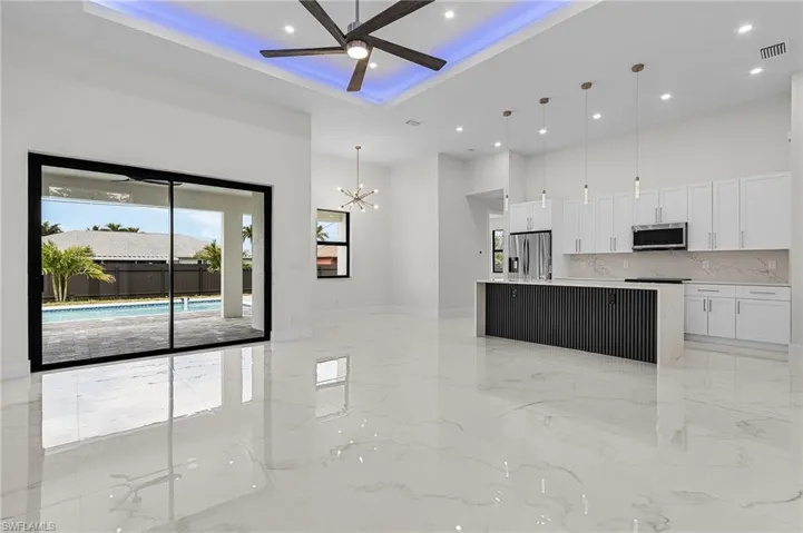 Kitchen with appliances with stainless steel finishes, porcelain floor, ceiling fan with notable chandelier, and a high ceiling