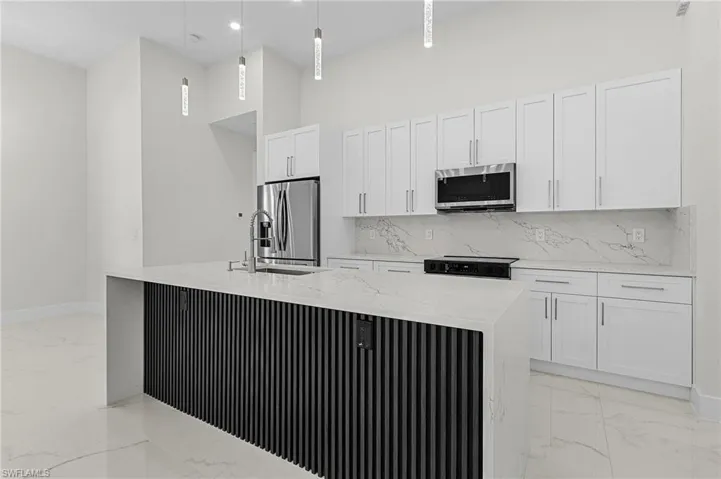 Kitchen featuring a kitchen island with sink, porcelain floors, white cabinetry, and appliances with stainless steel finishes