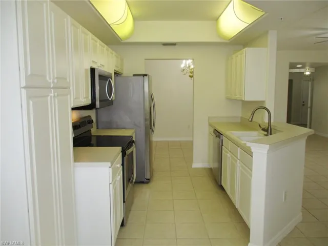 Kitchen featuring kitchen peninsula, light tile floors, sink, white cabinets, and appliances with stainless steel finishes