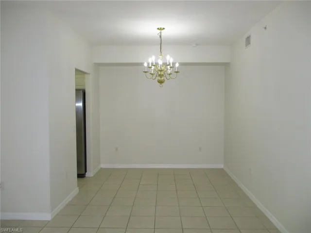 Unfurnished room featuring a notable chandelier and light tile floors