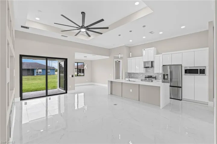 Kitchen with open floor plan, stainless steel appliances, white cabinetry, a kitchen island with sink, and hanging light fixtures