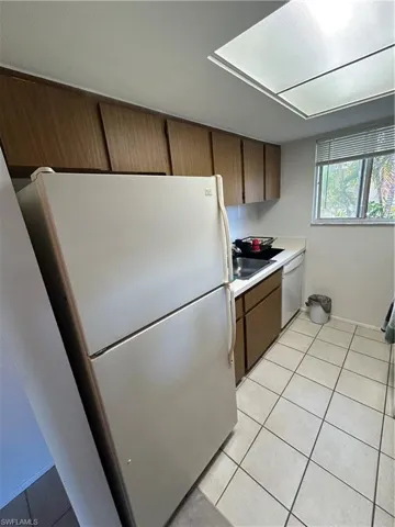 Kitchen with sink, light tile patterned floors, dishwashing machine, and white refrigerator