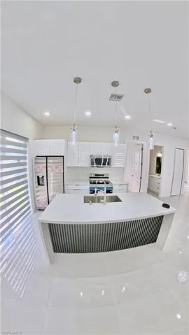 Kitchen featuring stainless steel appliances, white cabinets, hanging light fixtures, light stone countertops, and a spacious island