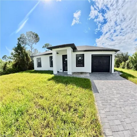 Prairie-style home with stucco siding, a front lawn, a garage, and decorative driveway