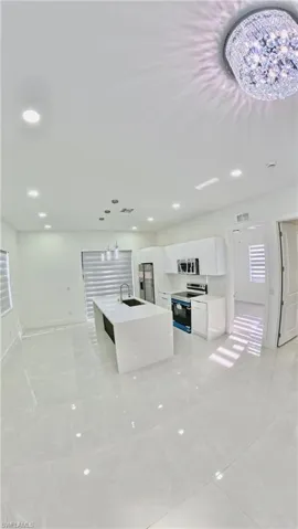 Kitchen featuring pendant lighting, stainless steel appliances, a center island with sink, white cabinets, and open floor plan
