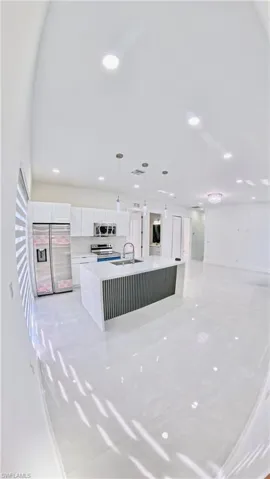 Kitchen featuring pendant lighting, appliances with stainless steel finishes, a center island with sink, white cabinetry, and open floor plan