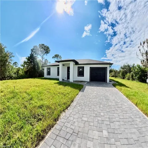 Prairie-style house with an attached garage, decorative driveway, a front lawn, and stucco siding