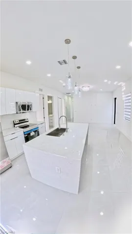 Kitchen with hanging light fixtures, a center island with sink, light stone counters, stainless steel appliances, and white cabinetry