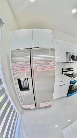 Kitchen with white cabinets, appliances with stainless steel finishes, light tile patterned floors, modern cabinets, and light stone countertops