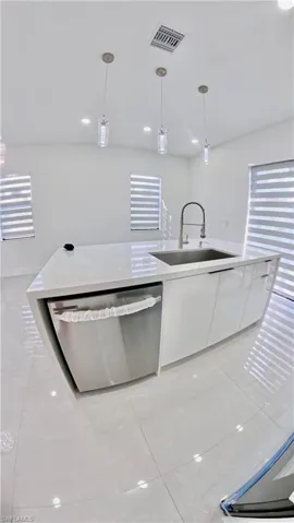 Kitchen with white cabinets, hanging light fixtures, light tile patterned floors, stainless steel dishwasher, and light stone countertops