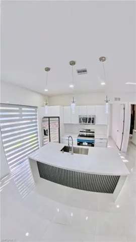 Kitchen featuring white cabinets, stainless steel appliances, decorative light fixtures, light stone counters, and a large island