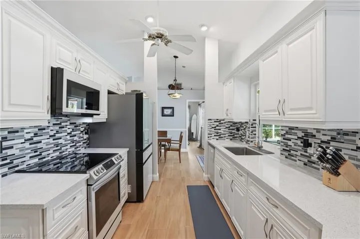 Kitchen featuring stainless steel appliances, white cabinets, light stone counters, vaulted ceiling, and a ceiling fan