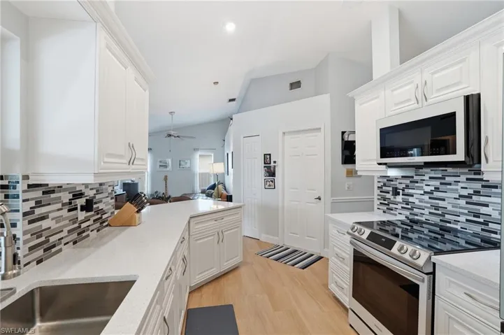Kitchen featuring stainless steel range with electric cooktop, lofted ceiling, white microwave, decorative backsplash, and white cabinetry