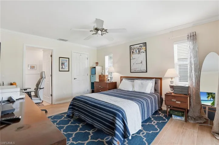 Bedroom with light wood tile floors, ornamental molding, an office area, and a ceiling fan