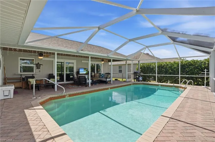 Swimming pool featuring an outdoor lounge area, screen enclosure, and a grill