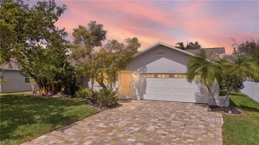 View of front of house with a yard, an attached garage, stucco siding, and decorative driveway