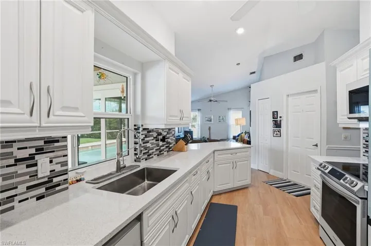 Kitchen featuring ceiling fan, electric range, light stone countertops, white cabinets, and lofted ceiling