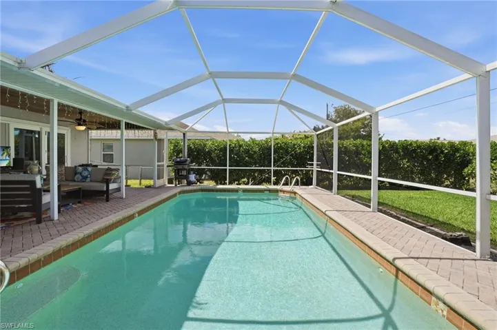 Swimming pool featuring an outdoor lounge area, screen enclosure, and a grill