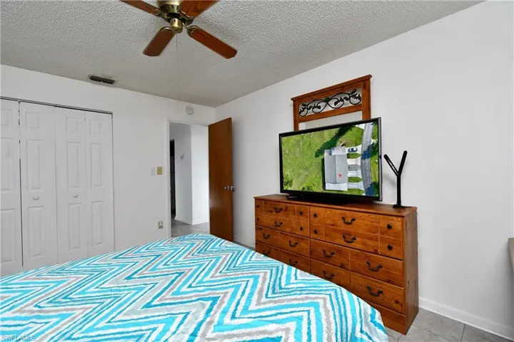 Bedroom with a textured ceiling, a closet, ceiling fan, tile patterned floors, and baseboards