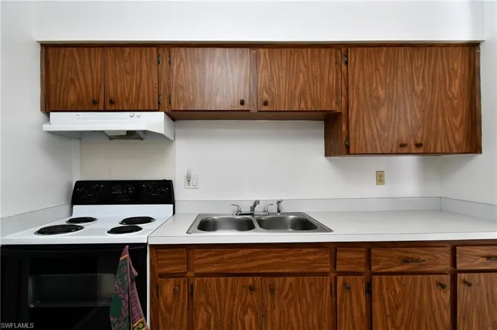 Kitchen featuring under cabinet range hood, electric stove, a sink, and light countertops