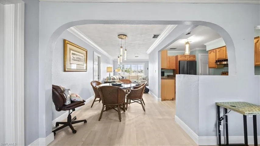 Dining area featuring arched walkways, light wood-style flooring, and crown molding