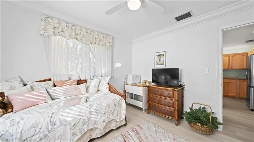 Bedroom with crown molding, light wood-style floors, freestanding refrigerator, and ceiling fan