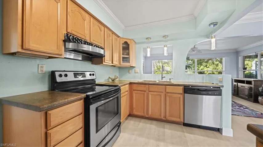 Kitchen with stainless steel appliances, hanging light fixtures, glass insert cabinets, crown molding, and a peninsula