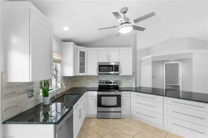 Kitchen with dark stone counters, white cabinetry, sink, appliances with stainless steel finishes, and backsplash
