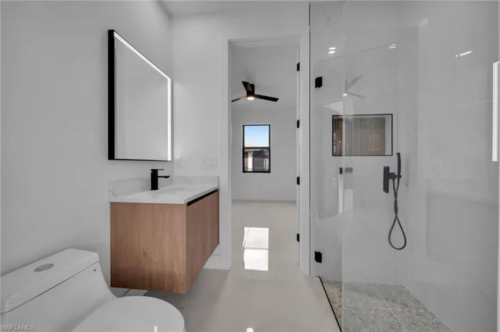 Bathroom featuring a marble finish shower, toilet, vanity, and ceiling fan
