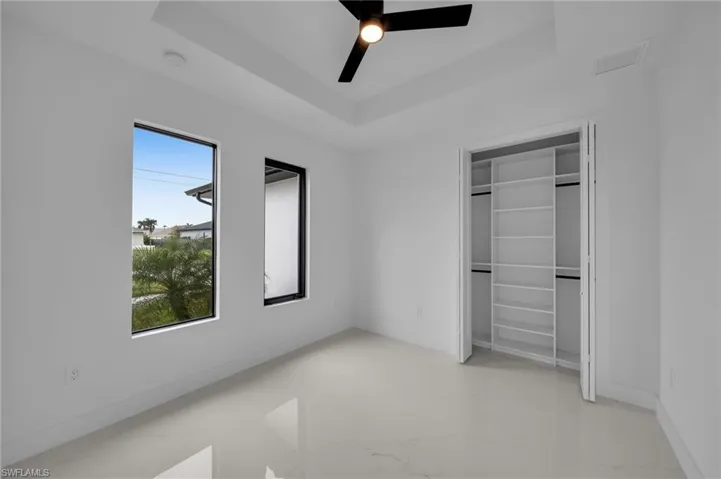 Unfurnished bedroom with a tray ceiling, baseboards, marble finish floor, and a ceiling fan