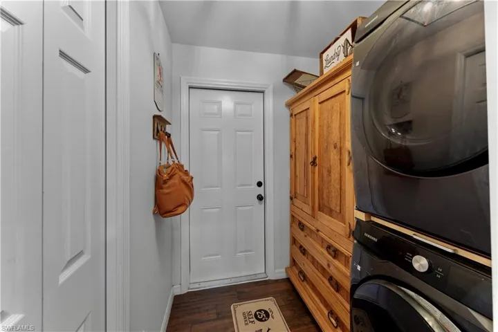 Laundry area featuring cabinet space, baseboards, dark wood-type flooring, and stacked washer / dryer