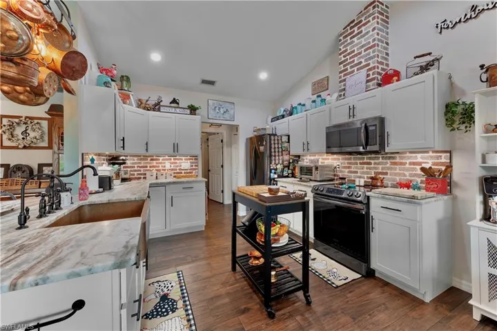 Kitchen featuring dark wood finished floors, stainless steel appliances, vaulted ceiling, a sink, and light stone countertops