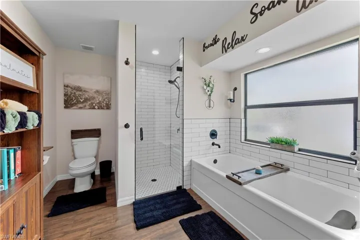 Bathroom with visible vents, toilet, a stall shower, wood finished floors, and a bath