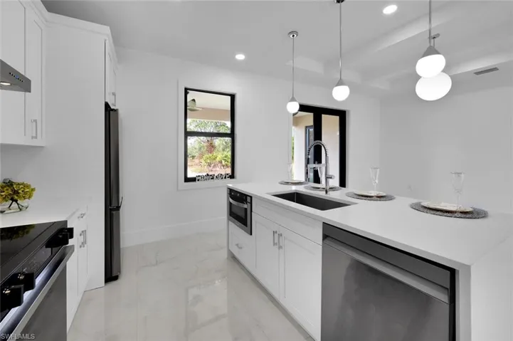 Kitchen featuring wall chimney exhaust hood, stainless steel appliances, sink, decorative light fixtures, and white cabinets