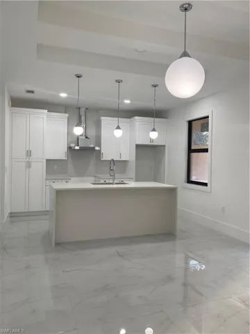 Kitchen with white cabinetry, sink, extractor fan, decorative light fixtures, and a kitchen island with sink