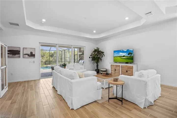 Living area with a sunroom, wood finish floors, a raised ceiling, and recessed lighting
