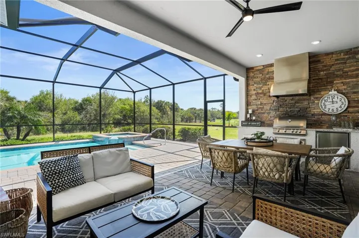 View of patio with a sunroom, exterior kitchen, a pool with connected hot tub, outdoor dining area, and a lanai