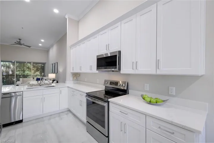 Kitchen featuring appliances with stainless steel finishes, light stone countertops, white cabinetry, ceiling fan, and crown molding