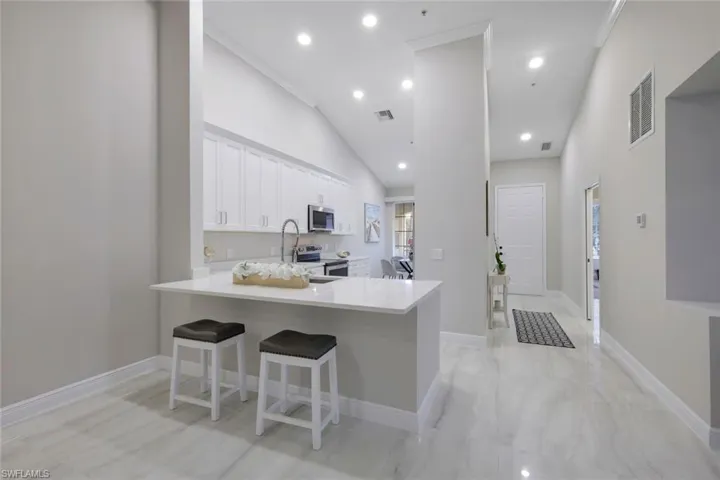 Kitchen featuring kitchen peninsula, a breakfast bar, white cabinets, appliances with stainless steel finishes, and high vaulted ceiling