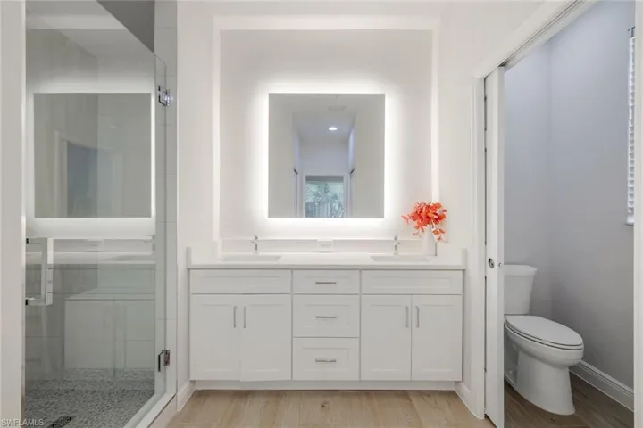 Bathroom with a shower with door, vanity, hardwood / wood-style floors, and toilet