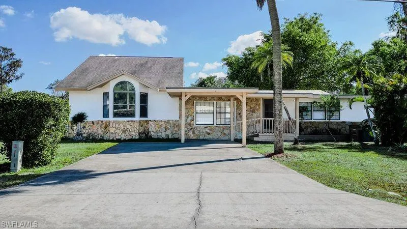Ranch-style home featuring stone siding, stucco siding, a front lawn, and covered porch